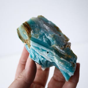 May include: A piece of raw, natural Amazonite gemstone. The stone displays a vibrant turquoise color with streaks of brown and white. The rough texture and unique patterns make it a striking specimen for collectors or jewelry makers.