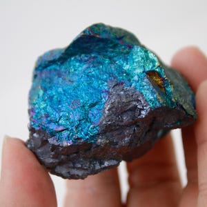 May include: A rough, iridescent blue and black mineral specimen with a metallic sheen. The mineral has a rough, uneven surface and is a natural, unpolished stone.