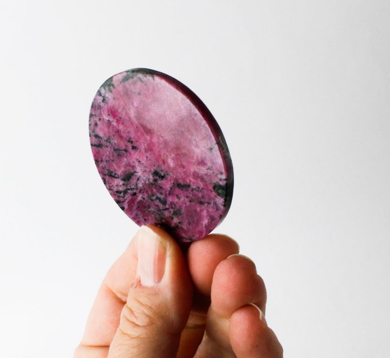May include: A round, pink and black, polished, natural stone with a marbled pattern.