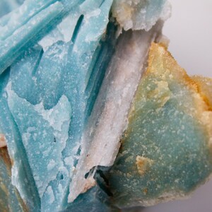 May include: Close-up of a mineral specimen featuring layered, crystalline structures. The dominant colors are shades of blue, with areas of white and touches of orange and brown. The texture appears rough and natural.