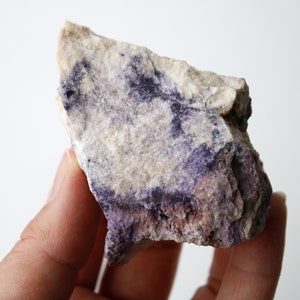 May include: A rough, irregular shaped rock with a white and purple color pattern. The rock has a rough, uneven texture.