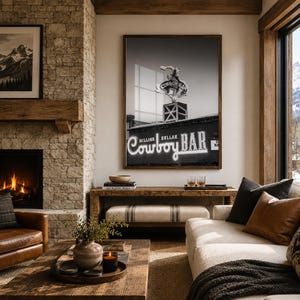 May include: A framed black and white wall art print featuring the iconic Million Dollar Cowboy Bar neon sign in Jackson Hole, Wyoming, with a bucking bronco silhouette atop the building structure, displayed in a dark wooden frame.