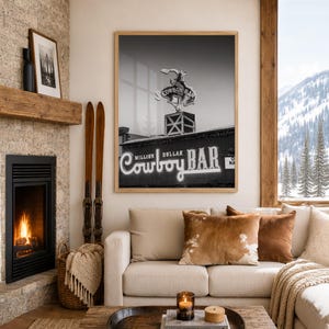 May include: A black and white framed wall art print featuring the Million Dollar Cowboy Bar sign with a bucking horse silhouette. The rectangular print is displayed in a light wood frame, showcasing the iconic neon signage and architectural details.
