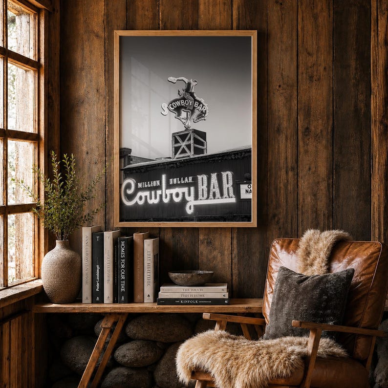 May include: A framed black and white wall art print featuring the Million Dollar Cowboy Bar sign with a neon cowboy figure on top. The text on the sign reads Million Dollar Cowboy Bar in a stylized script font, set against a dark background.
