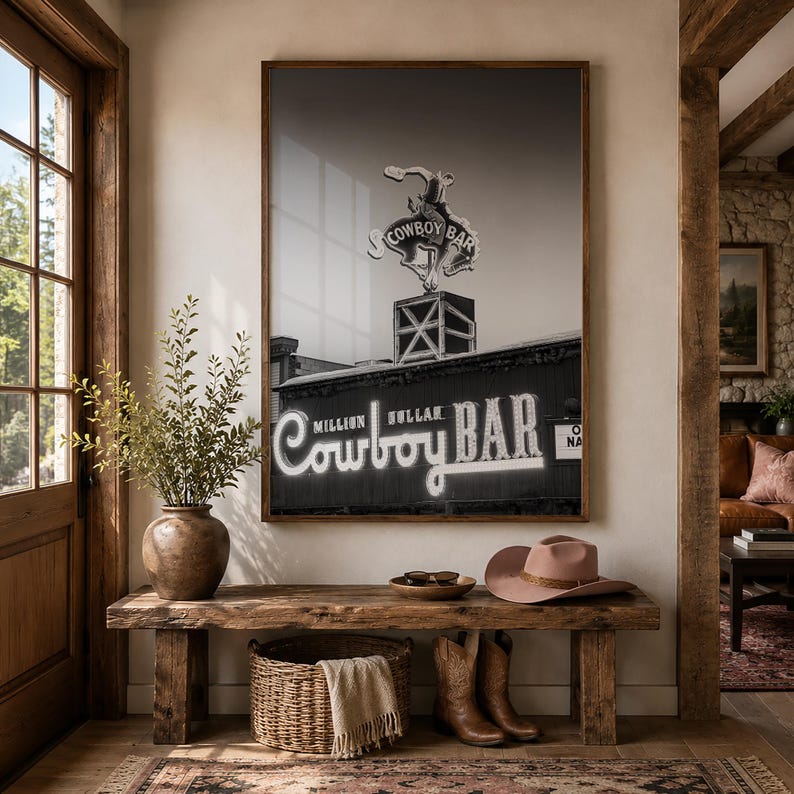 May include: A framed black and white wall art print depicting the Million Dollar Cowboy Bar sign with a bucking bronco silhouette. The artwork features the text Million Dollar Cowboy Bar in a stylized neon-style font, displayed in a dark wooden frame.