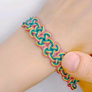May include: A braided bracelet with pink, yellow, and teal threads woven together in a complex pattern.
