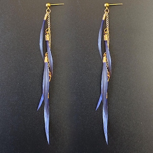 May include: A pair of dangle earrings with a gold-colored post and chain. The earrings feature three long, slender, blue-purple feather-like elements. The earrings are designed to hang down from the ear.