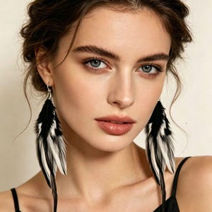 May include: Black and white feather earrings. The earrings are long and dangle, with a silver hook. The feathers are a mix of black and white, creating a striking contrast. The earrings are worn by a person with fair skin and dark hair.