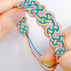 May include: A colorful braided bracelet with pink, yellow, and teal threads woven together in a complex knot pattern.