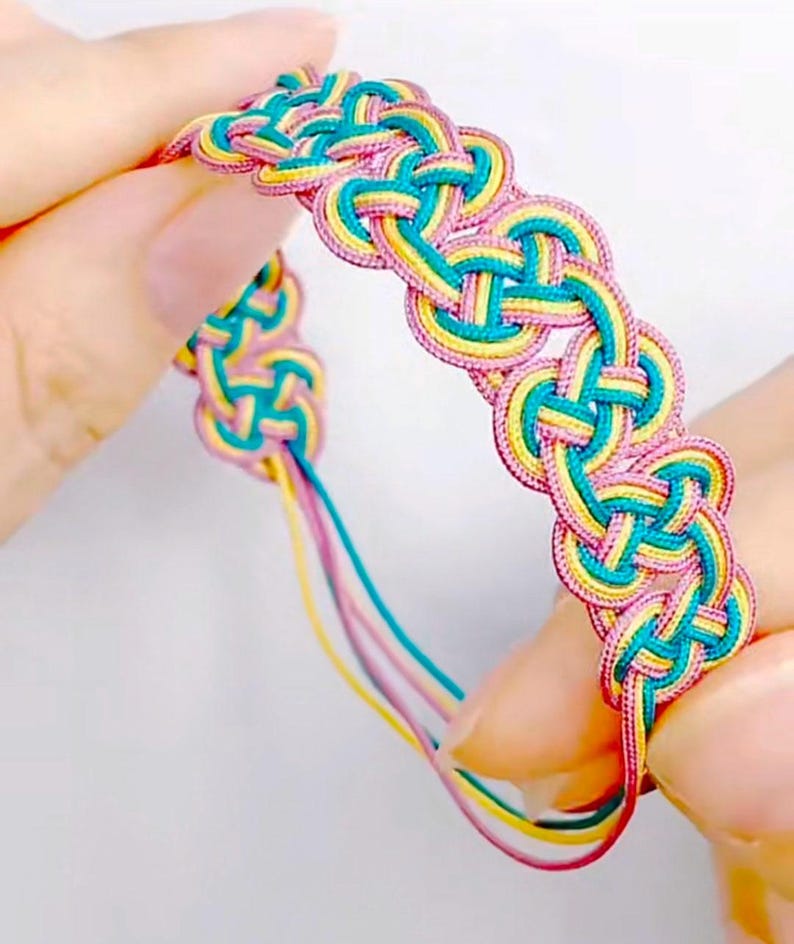 May include: A colorful braided bracelet with pink, yellow, and teal threads woven together in a complex knot pattern.