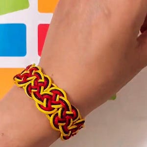 May include: A black, red, and yellow braided bracelet. The bracelet is made of woven string and is worn on a person's wrist.