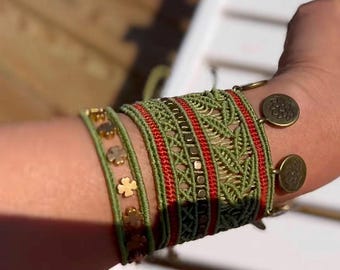 May include: A set of four bracelets with green and red woven patterns and gold accents. The bracelets are layered on a person's wrist.