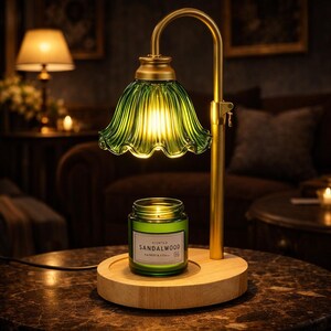 May include: A decorative table lamp with a green glass shade and a brass-colored metal frame. The lamp features a wooden base and a jar of scented sandalwood candle. The lamp is lit, casting a warm glow.