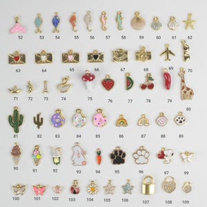 Puede incluir: Una colecci&oacute;n de peque&ntilde;os dijes coloridos con detalles dorados. Los dijes presentan varios dise&ntilde;os, incluyendo animales, comida y formas. Los dijes est&aacute;n numerados del 52 al 109.