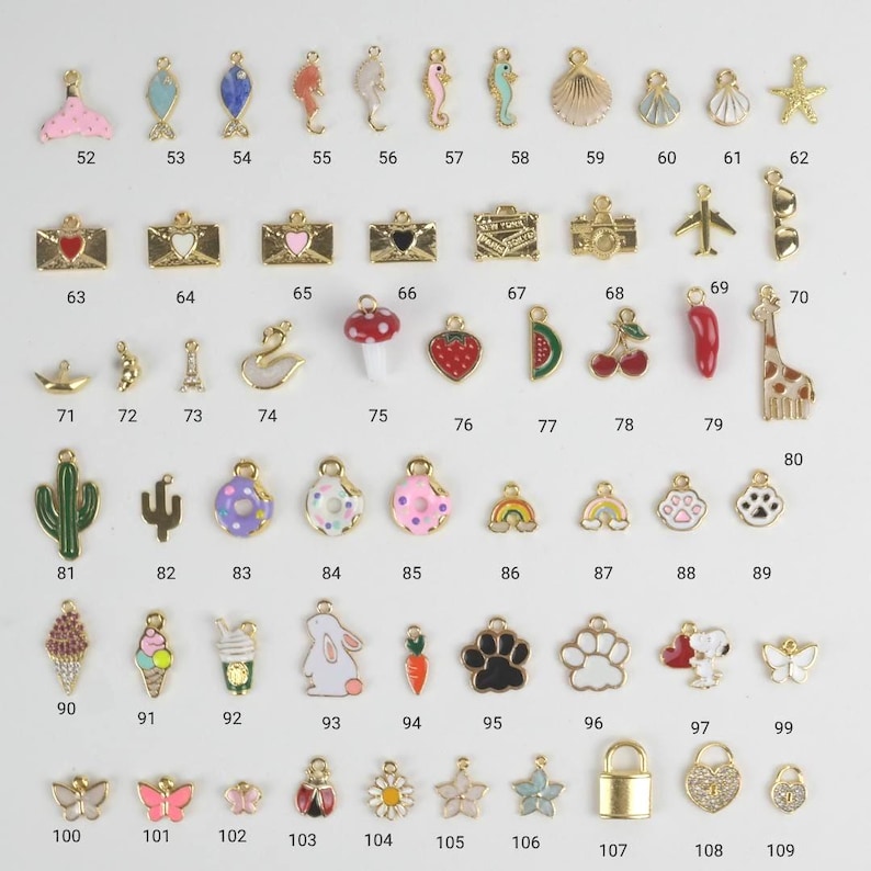 Puede incluir: Una colecci&oacute;n de peque&ntilde;os dijes coloridos con detalles dorados. Los dijes presentan varios dise&ntilde;os, incluyendo animales, comida y formas. Los dijes est&aacute;n numerados del 52 al 109.
