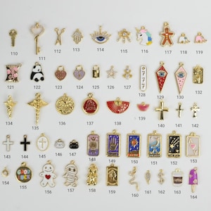 Puede incluir: Una colecci&oacute;n de dijes dorados, que incluyen llaves, cruces y varias formas como corazones, estrellas y un panda. Algunos dijes presentan detalles de esmalte y texto, como "Good Luck" y "Coffee".