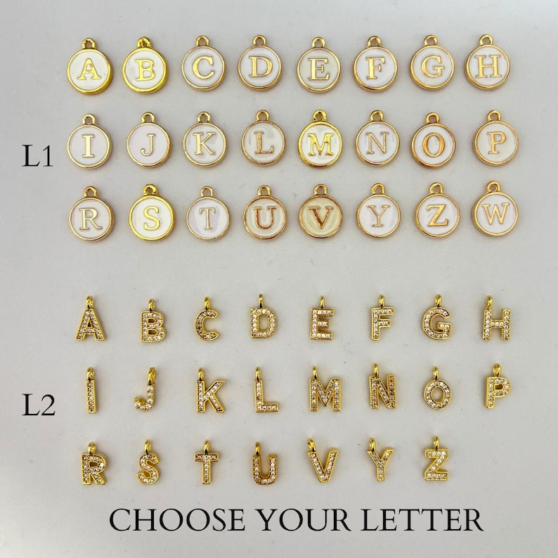 Puede incluir: Una selecci&oacute;n de colgantes de letras doradas, algunos con fondos de esmalte blanco y otros incrustados con peque&ntilde;os cristales transparentes. El texto "CHOOSE YOUR LETTER" est&aacute; en la parte inferior. Ideal para joyer&iacute;a personalizada.