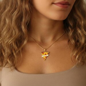May include: A gold-colored necklace with a pizza slice pendant. The pendant features a yellow crust, red pepperoni, and a banner that reads "TRUE LOVE". The necklace is worn on a person.