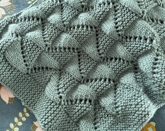 May include: A soft, sage green knitted blanket with a textured, diamond-shaped pattern.