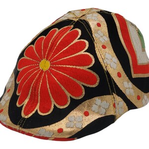 May include: A black, gold, and red patterned newsboy cap with a large red flower design.