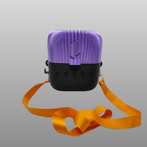 May include: A rectangular carrying case with a purple top section and a black bottom section featuring the embossed text PROXY. The case includes a bright orange nylon strap attached to silver metal hardware on both sides of the container.