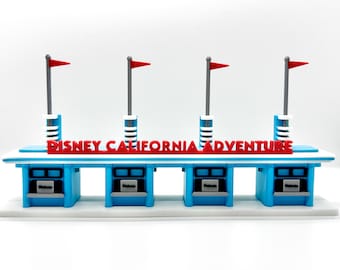 Könnte beinhalten: Ein Miniaturmodell der Ticket-Schalter von Disney California Adventure. Das Modell zeigt vier blaue Ticketschalter mit weißen Zierleisten, roten Fahnen und den Worten "DISNEY CALIFORNIA ADVENTURE" in roten Buchstaben.