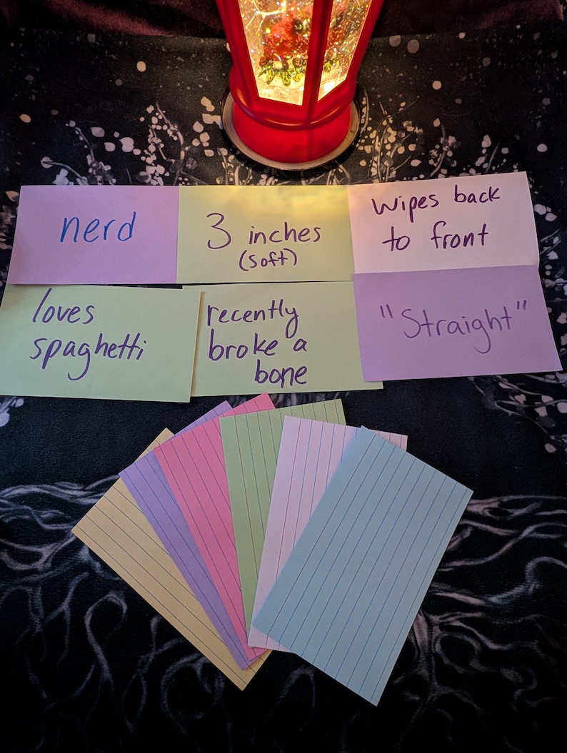 May include: A set of eight index cards with handwritten text. The cards are in various colors, including yellow, green, pink, purple, and blue. The text on the cards includes "nerd", "loves spaghetti", "3 inches (soft)", "recently broke a bone", "wipes back to front", and "'Straight'".