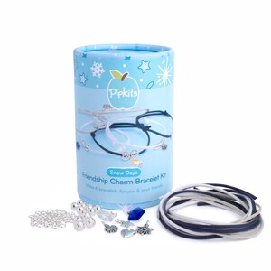 Könnte beinhalten: Eine blaue und weiße zylindrische Box mit dem Text "Pipkits Snow Days Friendship Charm Bracelet Kit Make 6 bracelets for you & your friends" auf der Vorderseite. Die Box enthält eine Vielzahl von silbernen Charms, Perlen und Schnüren zum Herstellen von Freundschaftsarmbändern.