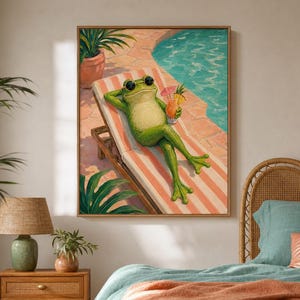 May include: A framed wall art print depicting a green frog wearing black sunglasses, lounging on a striped beach chair beside a swimming pool. The frog holds a tropical drink with a small umbrella, set against a background of pool water.