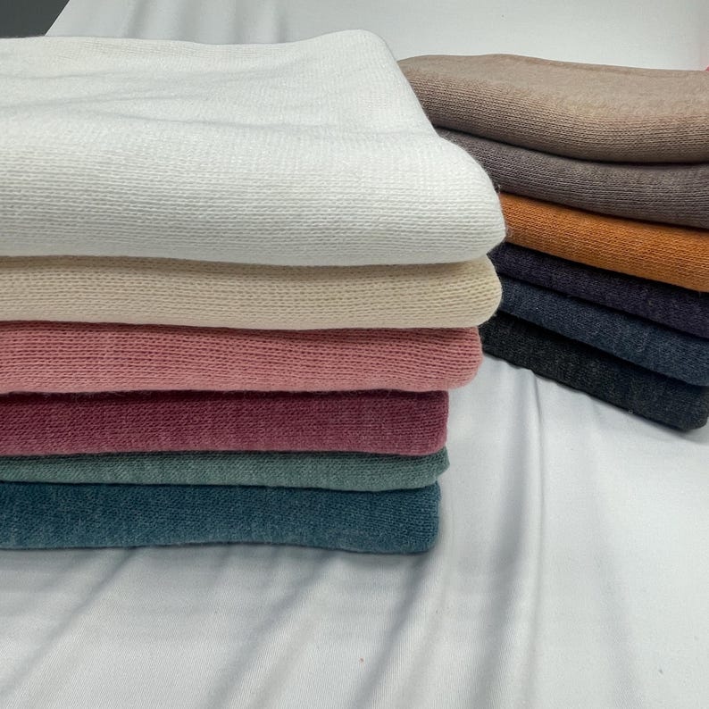 May include: A stack of eight fabric swatches in various colors, including white, beige, pink, burgundy, teal, and gray. The swatches are folded and stacked on top of each other.