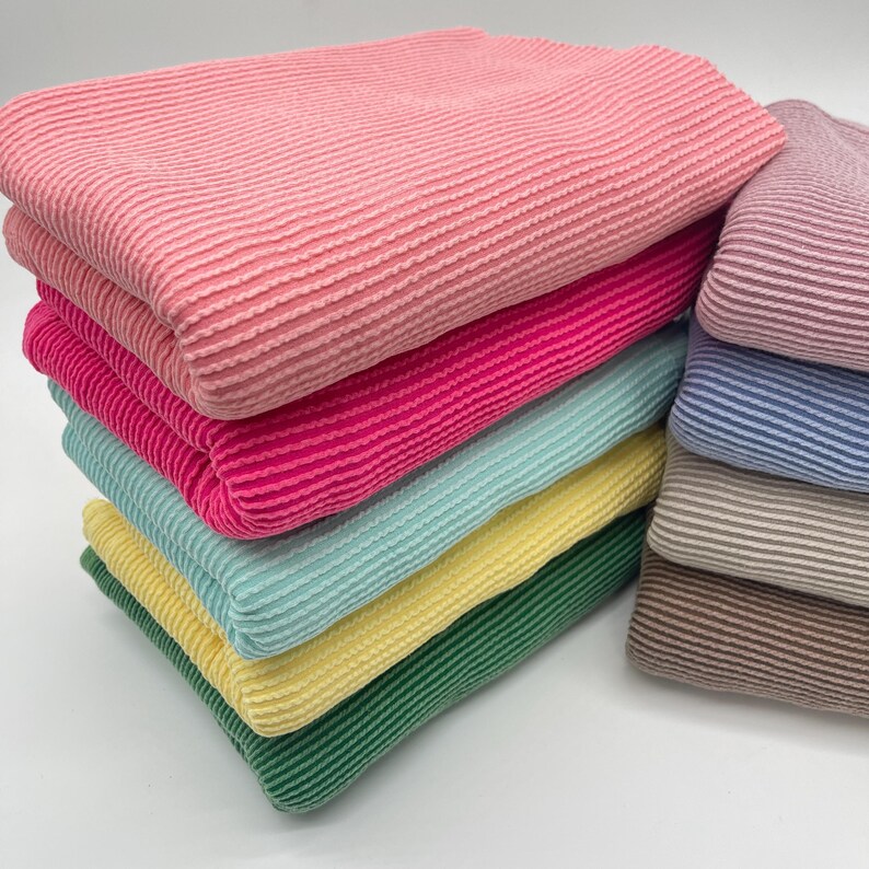 Two stacks of folded, ribbed knit fabric, with the left stack in bright colors and the right stack in muted colors, on a white background.