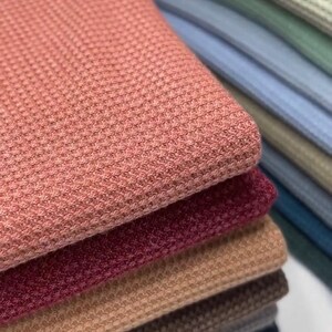 May include: A stack of waffle knit fabric in various colors, including pink, red, brown, beige, and gray.