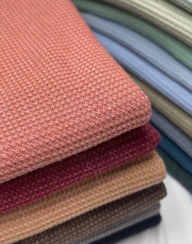 May include: A stack of waffle knit fabric in various colors, including pink, red, brown, beige, and gray.