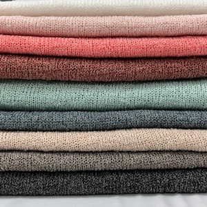 May include: A stack of eight different colored knitted fabrics. The fabrics are arranged in a rainbow pattern, starting with white and ending with dark gray.