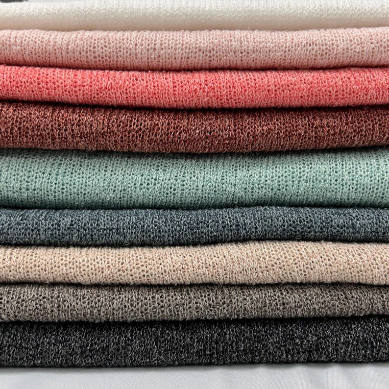 May include: A stack of eight different colored knitted fabrics. The fabrics are arranged in a rainbow pattern, starting with white and ending with dark gray.
