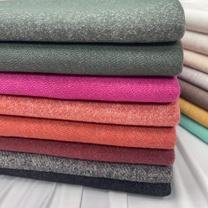 A stack of folded French terry fabrics in various colors including green, pink, coral, red, grey, and black.