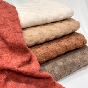 May include: A stack of folded fabric in various neutral colors, including cream, tan, brown, and rust. The fabric has a woven, textured pattern. The image is well-lit, highlighting the different shades and textures of the material.