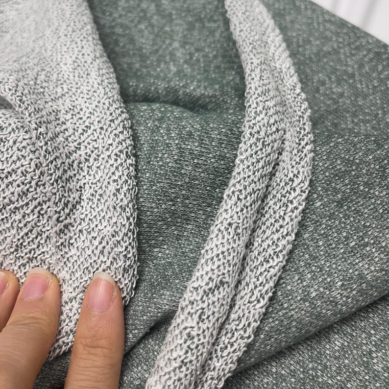 Close up of green French terry fabric showing the smooth outer face and looped interior texture, with fingers holding the fabric.