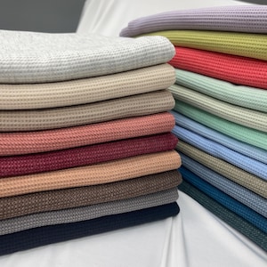 May include: A stack of waffle knit fabric in various colors, including gray, beige, pink, red, brown, and blue.