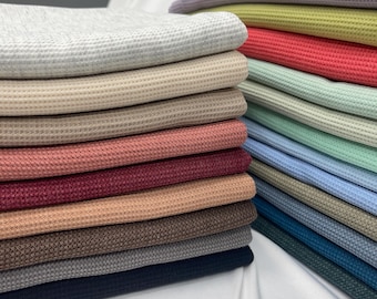 Peut inclure: Une pile de tissu en maille gaufrée de différentes couleurs, notamment gris, beige, rose, rouge, marron et bleu.