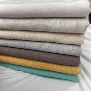A stack of folded French terry fabrics in neutral tones, yellow, and turquoise.