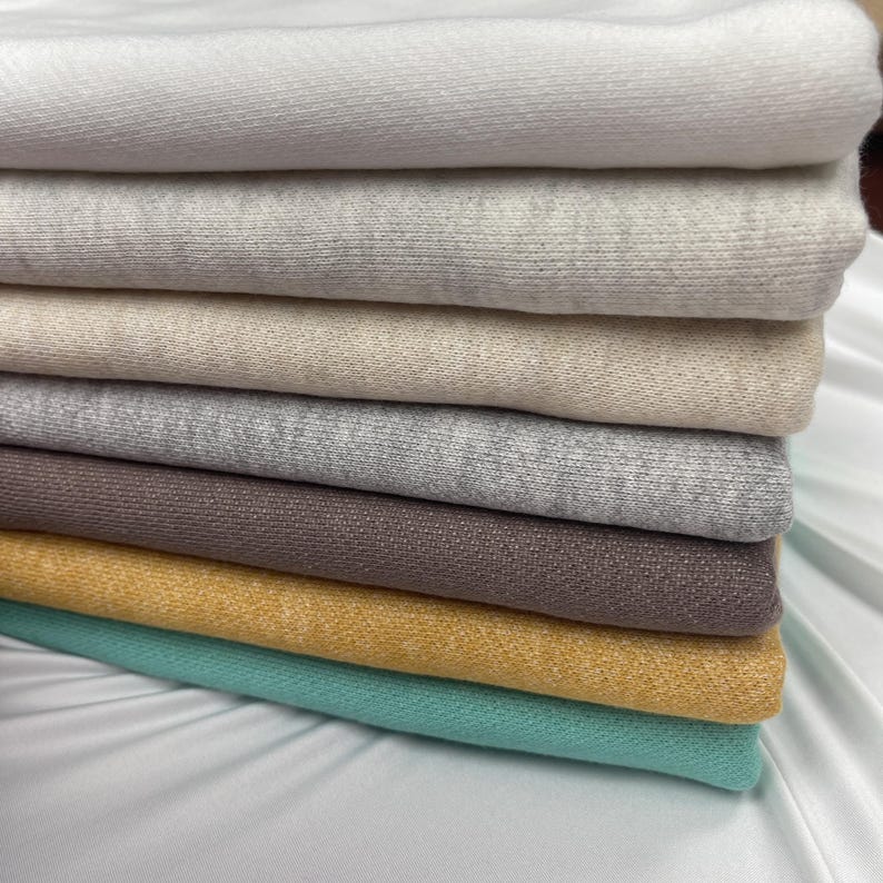 A stack of folded French terry fabrics in neutral tones, yellow, and turquoise.