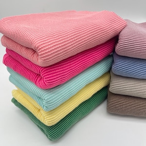 Two stacks of folded, ribbed knit fabric, with the left stack in bright colors and the right stack in muted colors.