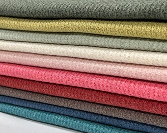 May include: A stack of fabric swatches in various colors, including green, yellow, beige, pink, red, brown, blue, and teal. The fabric has a ribbed texture.