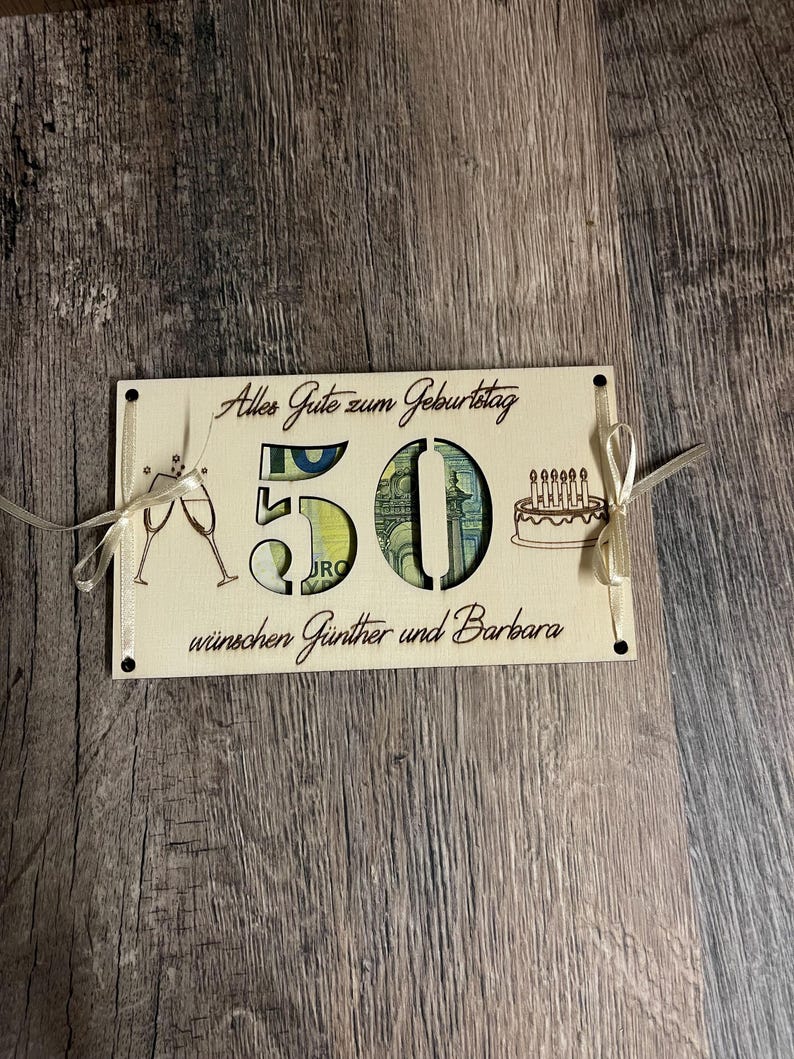 May include: A light-colored wooden birthday card with the number 50 cut out, revealing a Euro bill. The card includes the text "Alles Gute zum Geburtstag" and "w&uuml;nschen G&uuml;nther und Barbara", along with champagne glasses and a cake.