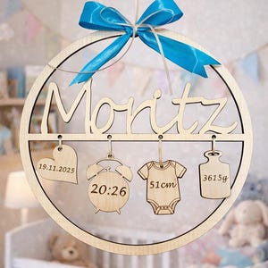 May include: A wooden baby announcement sign with the name "Moritz" in cursive. The sign includes a blue ribbon and hanging wooden cutouts with the baby's birthdate, time, length (51cm), and weight (3615g).