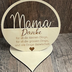 Könnte beinhalten: Holzschilder mit herzförmigem Sockel und runder Aussparung. Das Schild trägt die Aufschrift "Mama Danke" und enthält den Text "für all die kleinen Dinge, für all die grossen Dinge, und alle Dinge dazwischen".
