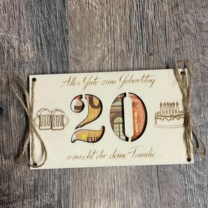 May include: A wooden birthday card with the number 20 cut out, filled with Euro banknotes. The card includes the text "Alles Gute zum Geburtstag" and a birthday cake illustration. Twine is used to hang the card.