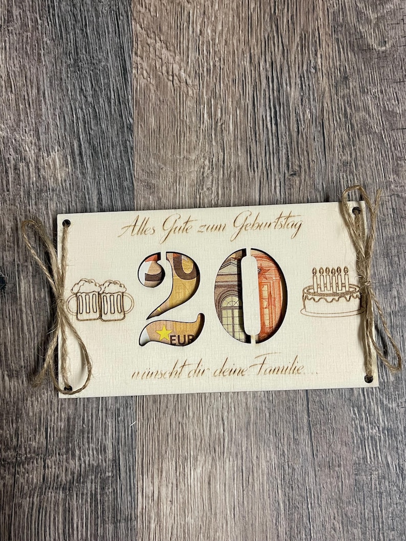 May include: A wooden birthday card with the number 20 cut out, filled with Euro banknotes. The card includes the text "Alles Gute zum Geburtstag" and a birthday cake illustration. Twine is used to hang the card.