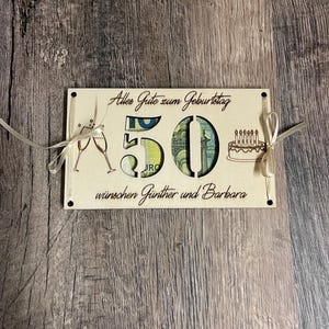 May include: A wooden birthday card with the number 50 cut out, filled with currency. The card has champagne glasses, a cake with candles, and the text "Alles Gute zum Geburtstag w&uuml;nschen G&uuml;nther und Barbara" in a decorative font.